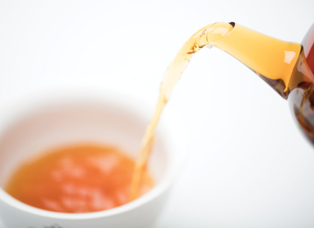 Glass teapot pouring tea into white teacup
