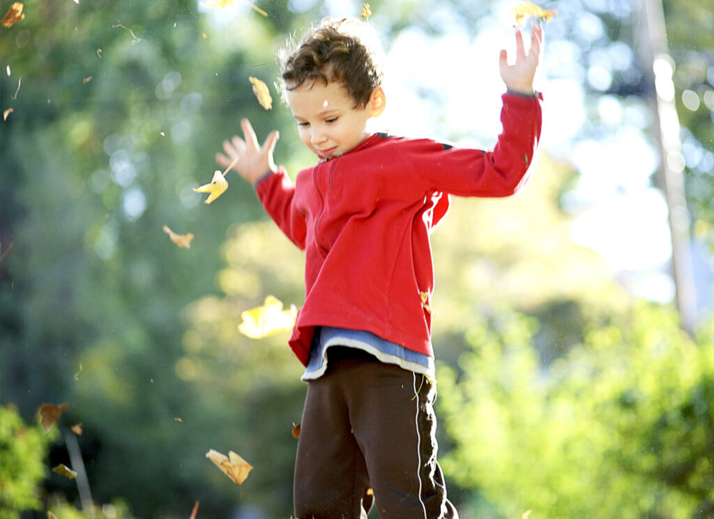 Young boy outside throwing leaves