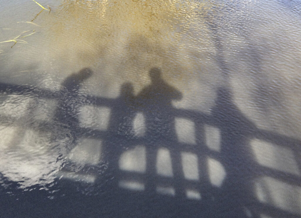 4 silhouettes on bridge reflected on water
