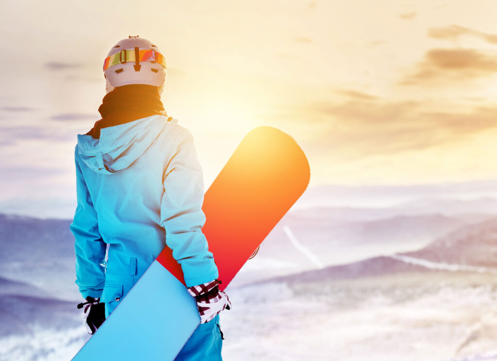 Person in blue snow gear carrying snowboard on snowy mountaintop