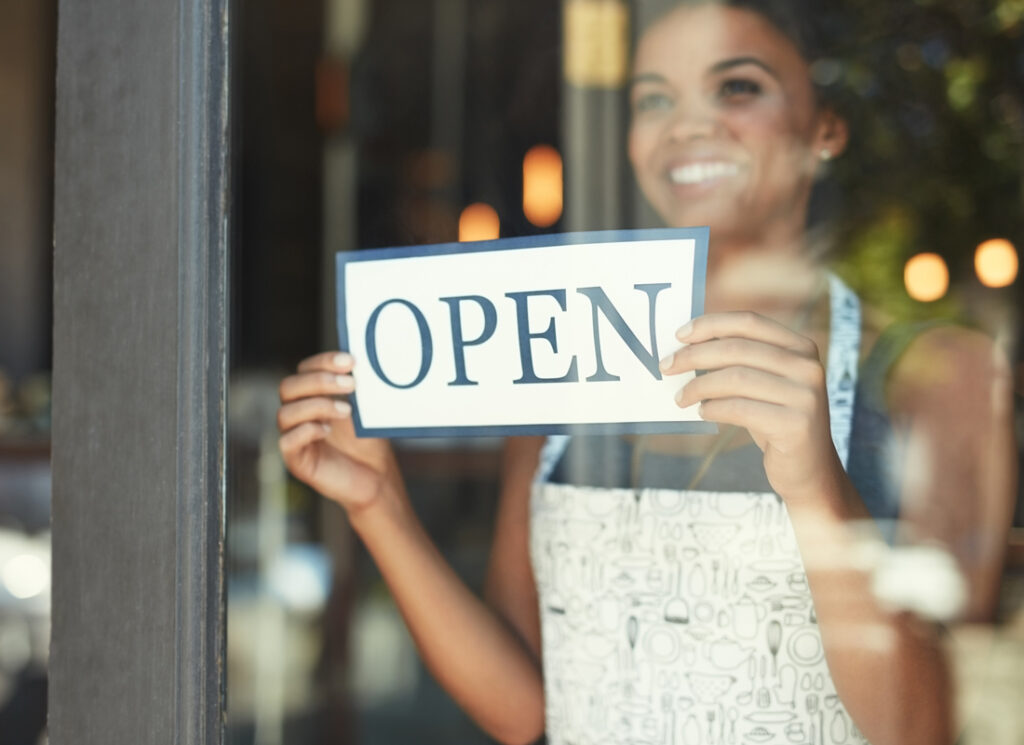 Woman in apron changing sign in business window to "open"