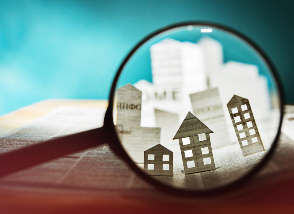 Magnifying glass showing tiny city made of newspaper