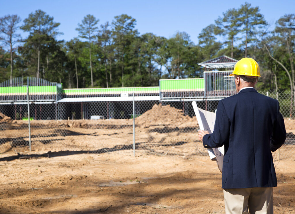 Man in hard hat holding blueprints at construction site