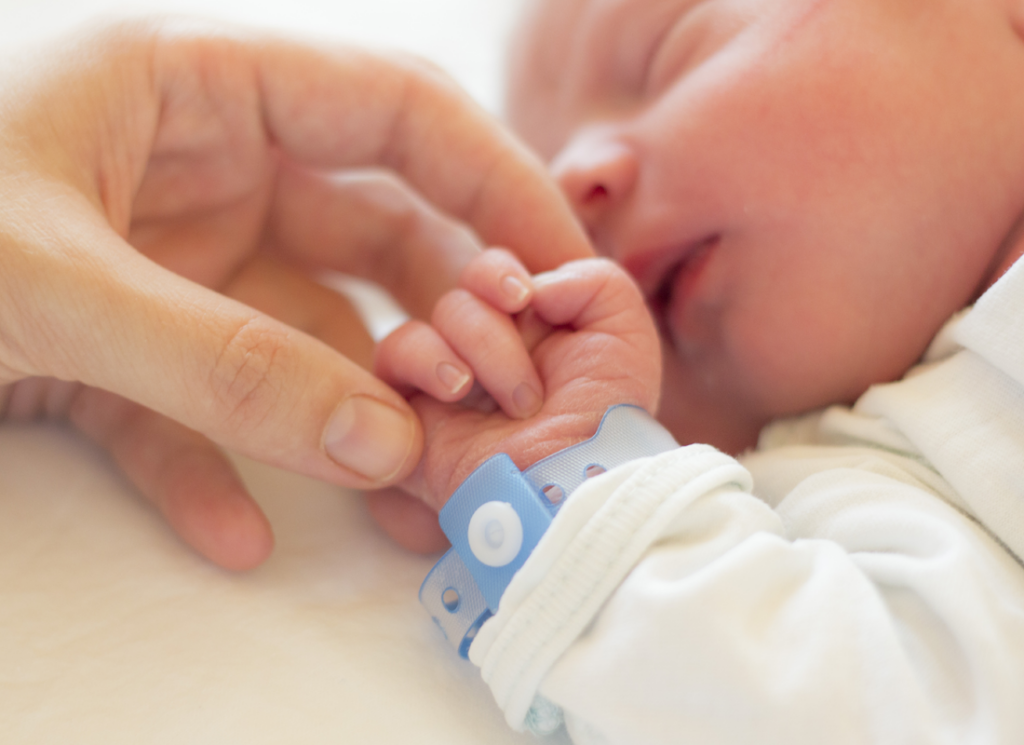 Adult holding hand of newborn baby wearing hospital bracelet